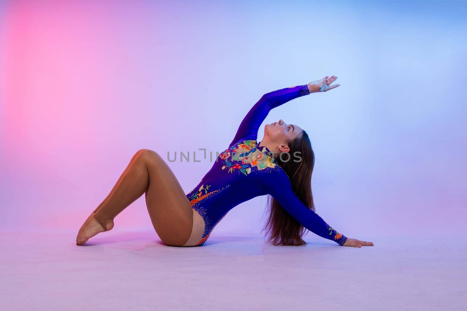 A girl gymnast in a swimsuit does tricks on white and dark background. Front view