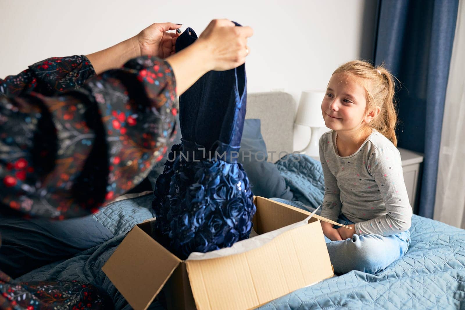 Mother and her daughter opening box with ordered dress at home on couch. Mom online shopper customer holding dress. Delivery service fashion concept