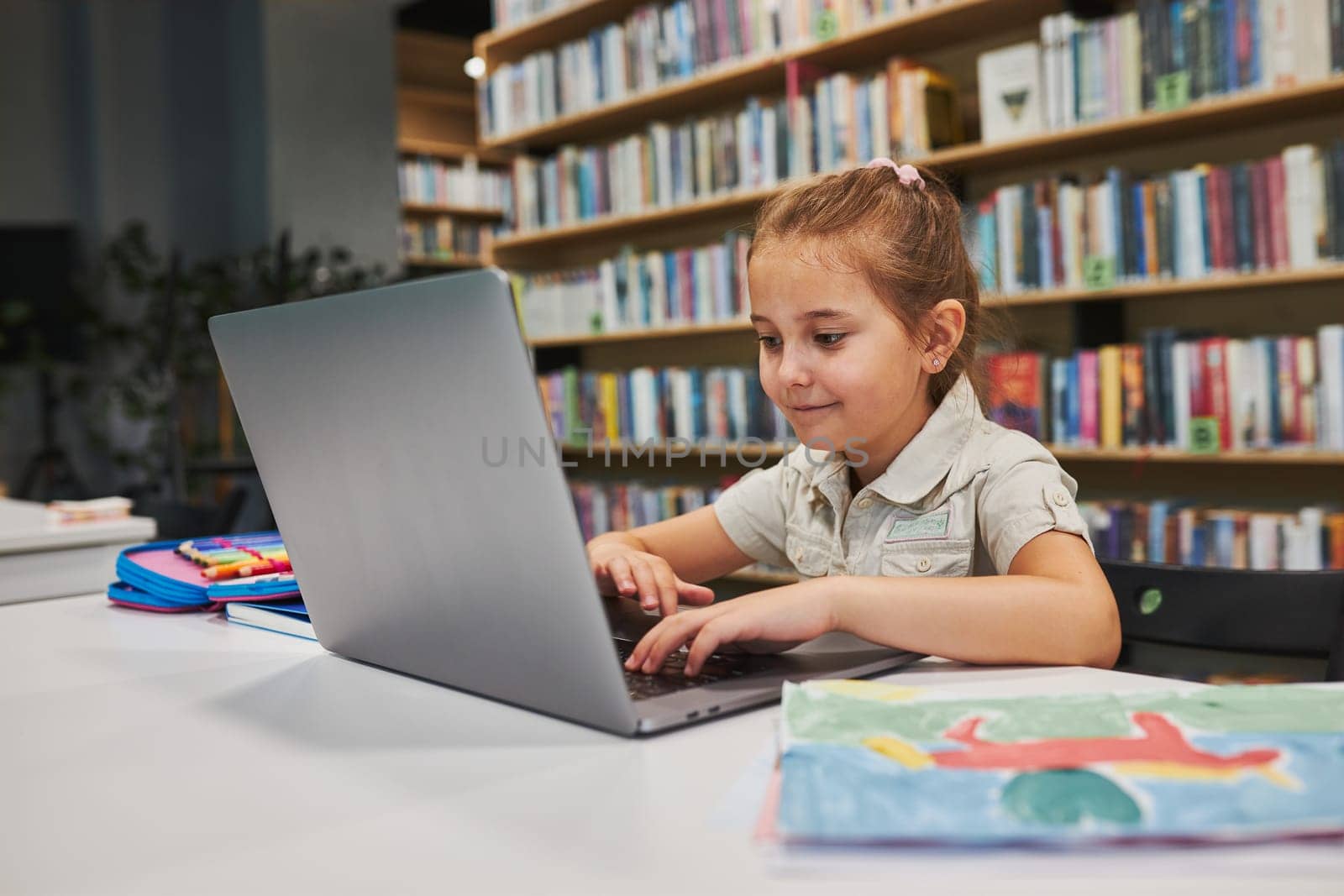 Positively engaged student doing her homework using laptop in after school club at primary school. Back to school. Child using technology on elementary computer science class. Smart little girl learning from educational application at school. Child solving riddles and puzzles on personal computer
