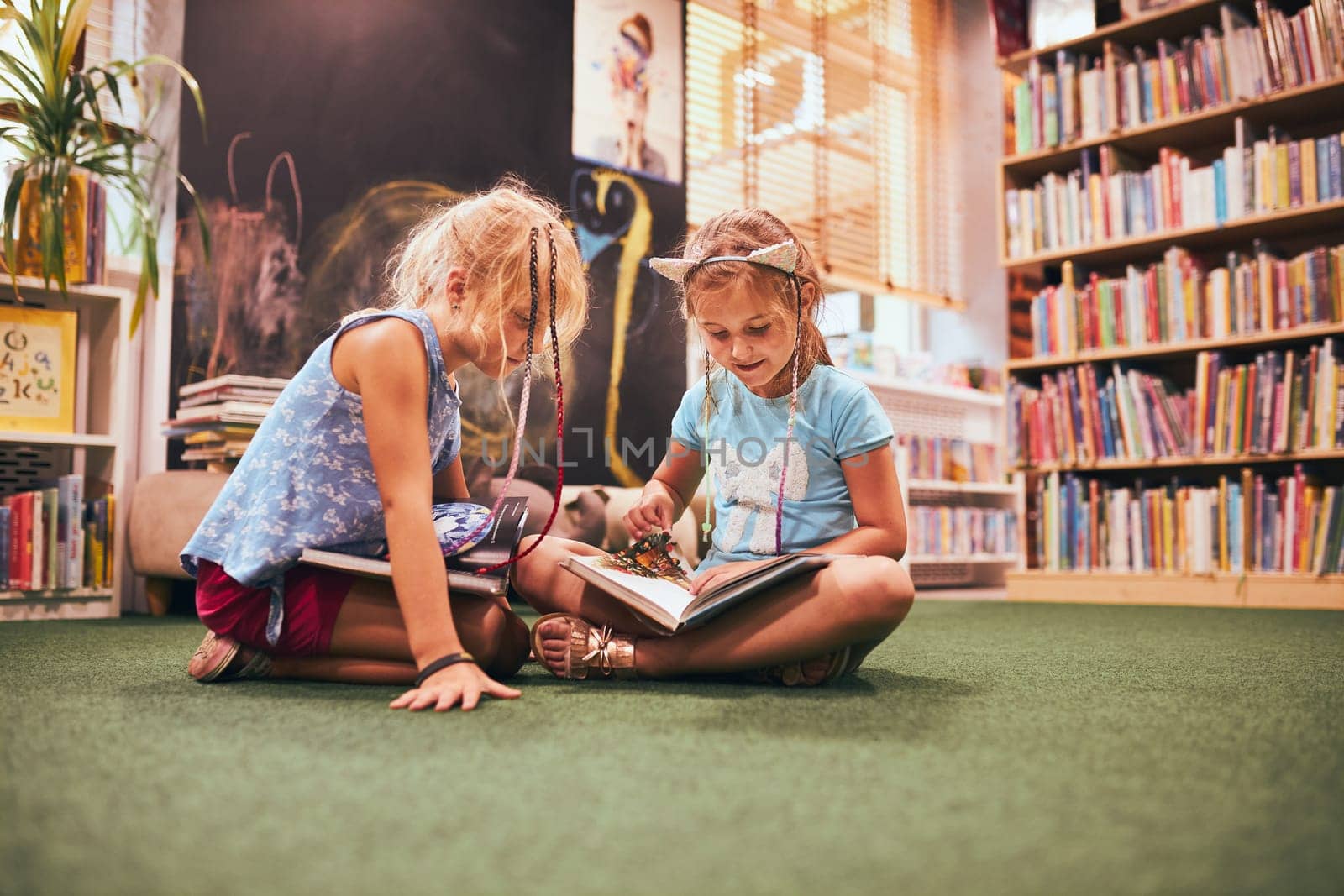 Two primary schoolgirls doing homework in school library. Students learning from books. Pupils having fun in library. Back to school