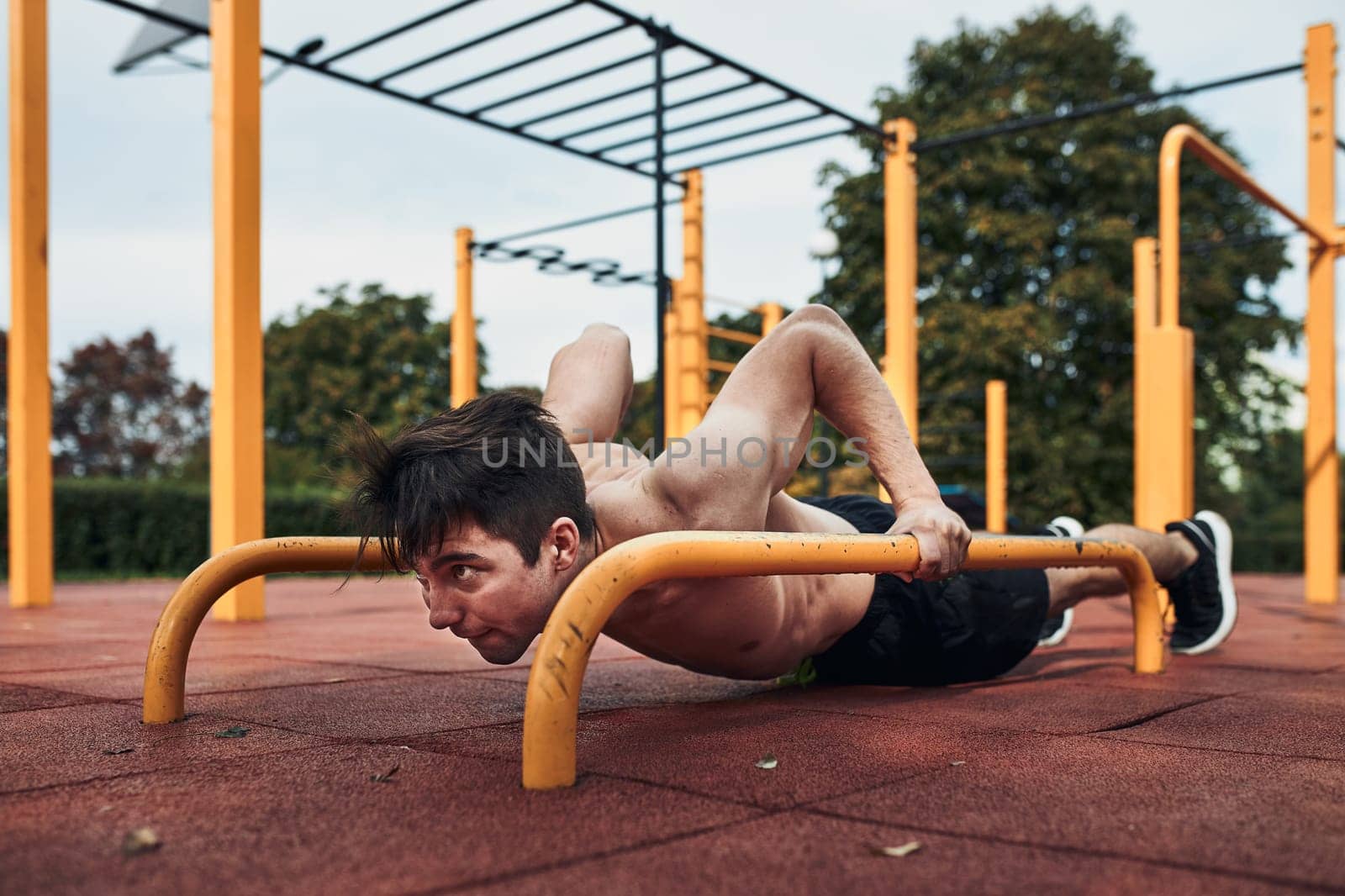 Young shirtless man bodybuilder doing push-ups on a parallel bars during his workout in a modern calisthenics street workout park