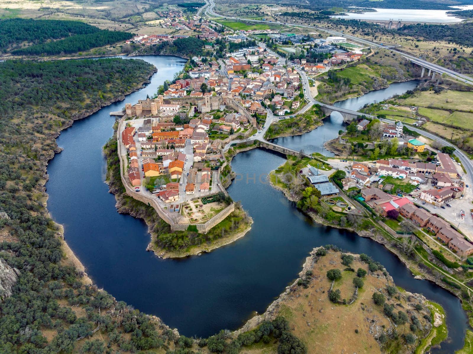Aerial view of Buitrago del Lozoya, a well preserved historic village near Madrid, surrounded by the Lozoya river, with the Guadarrama mountain chain and reservoir in the background. Long exposure.