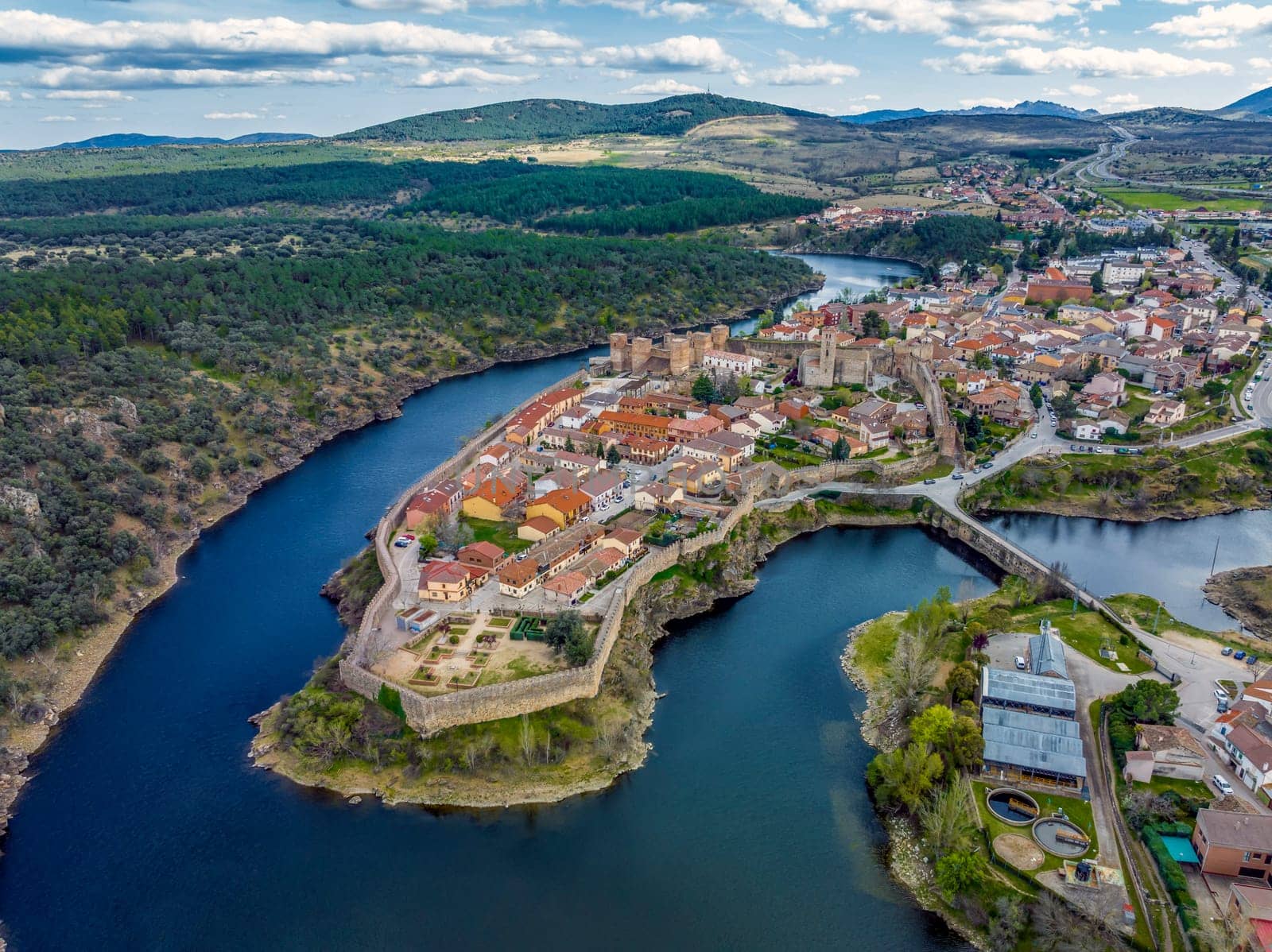 Aerial view of Buitrago del Lozoya, a well preserved historic village near Madrid, surrounded by the Lozoya river, with the Guadarrama mountain chain and reservoir in the background. Long exposure.