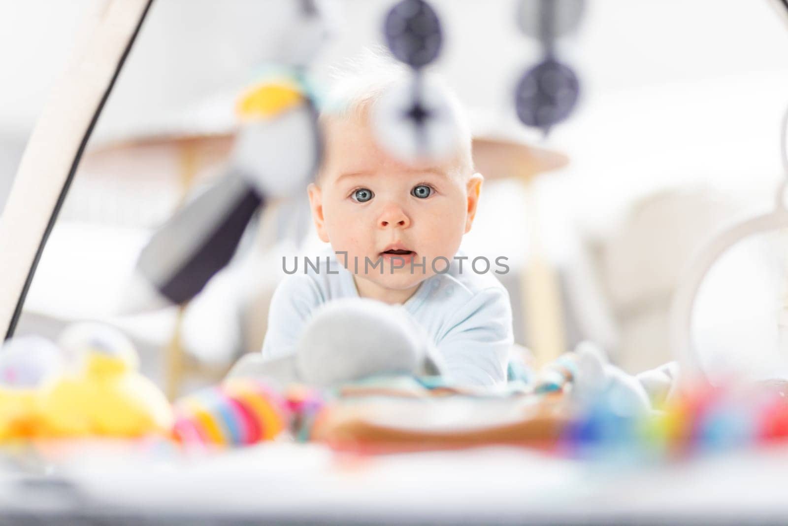 Cute baby boy playing with hanging toys arch on mat at home Baby activity and play center for early infant development. Baby playing at home.