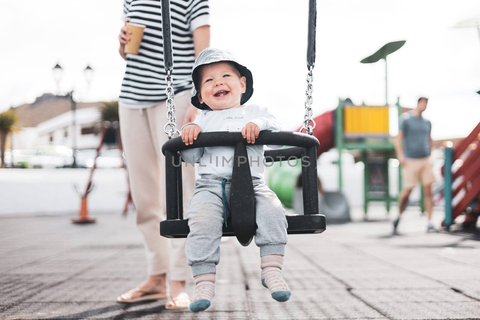 Mother pushing her infant baby boy child on a swing on playground outdoors