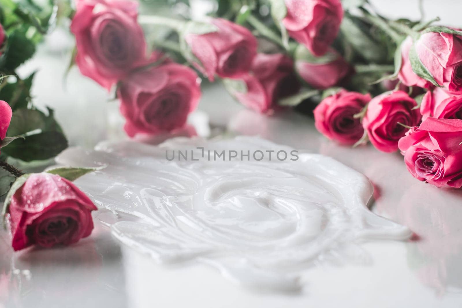 White cream smeared on glossy surface surrounded by blurred delicate pink roses