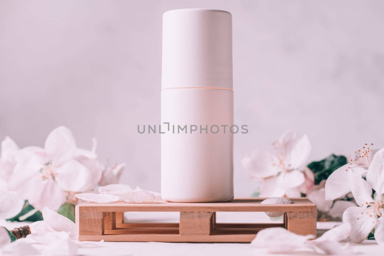 Antiperspirant roll-on deodorant on wooden podium in form of pallet on light plaster surface with apple flowers