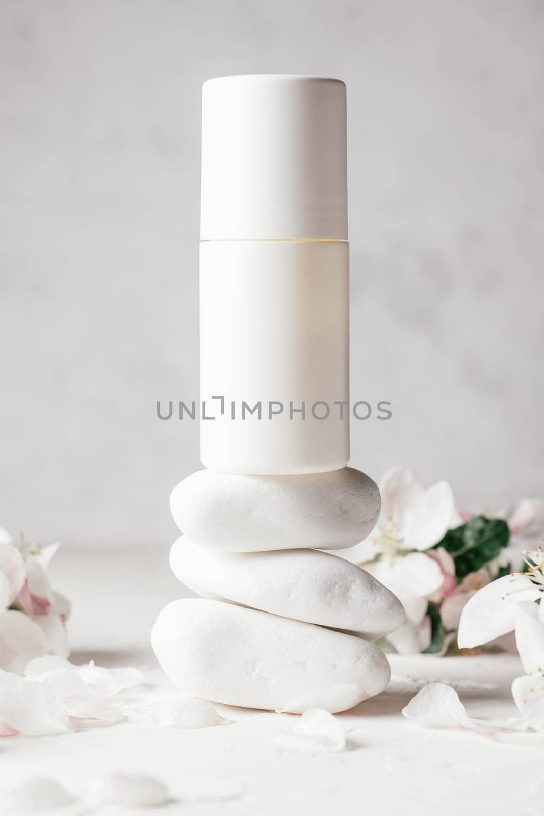 Antiperspirant roll-on deodorant on stack of white pebble stones on light plaster surface with apple flowers