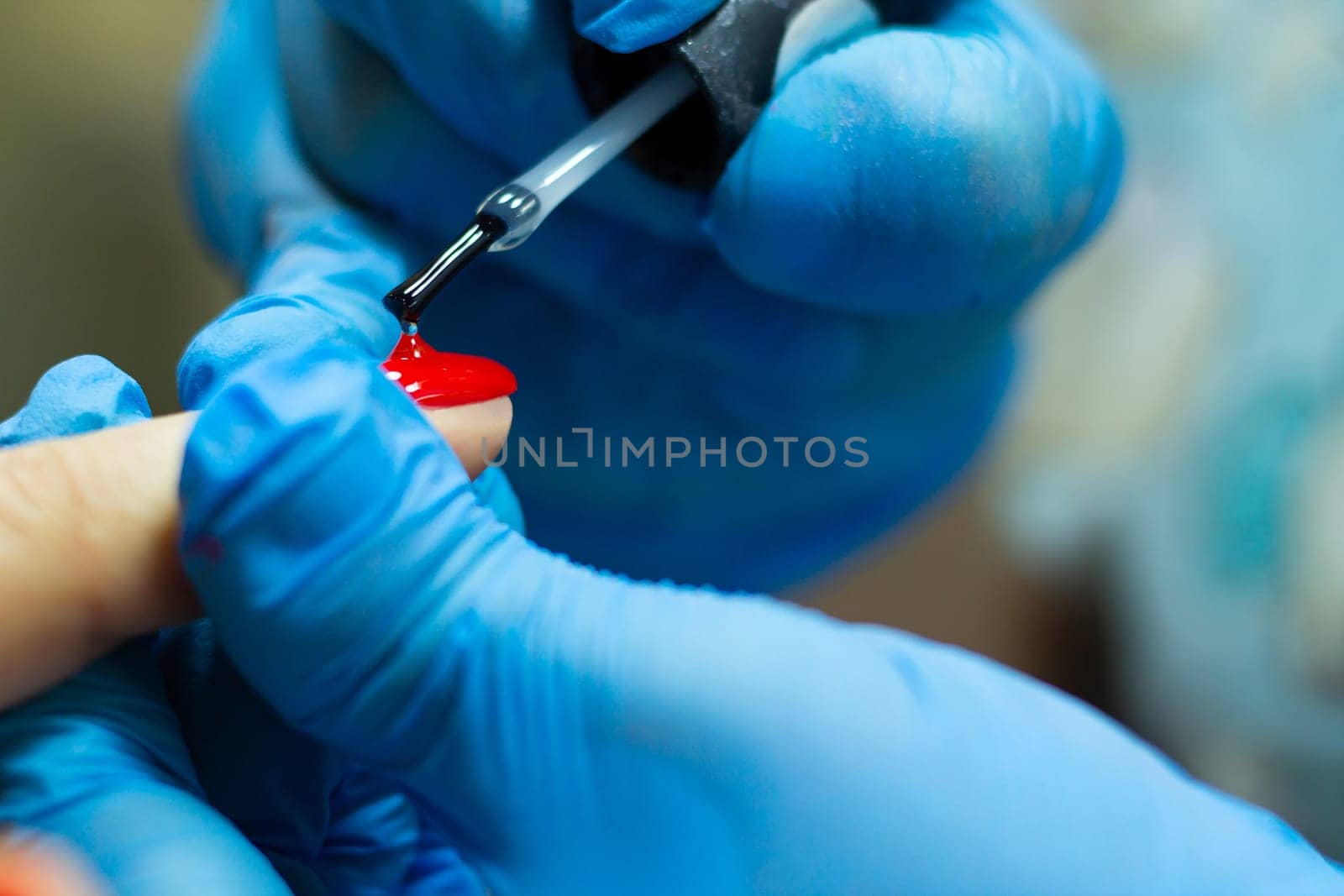 A manicurist in blue gloves, covering the nails with a long-lasting red gel polish.