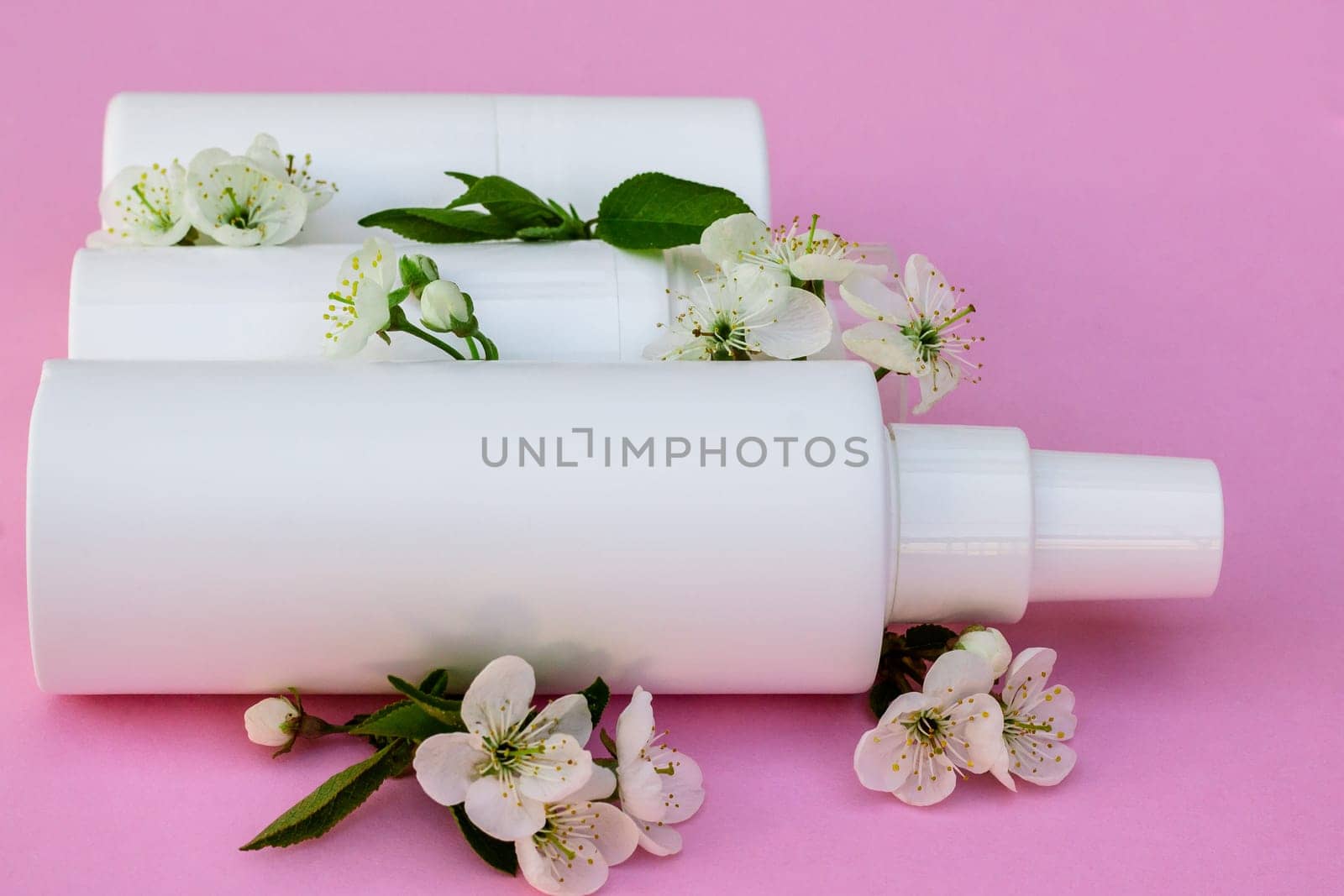 White cosmetic bottles, bath bomb, handmade soap, bath salt, massage brush, sponge, cotton buds with cherry flowers on a pink background. Natural organic cosmetics concept.