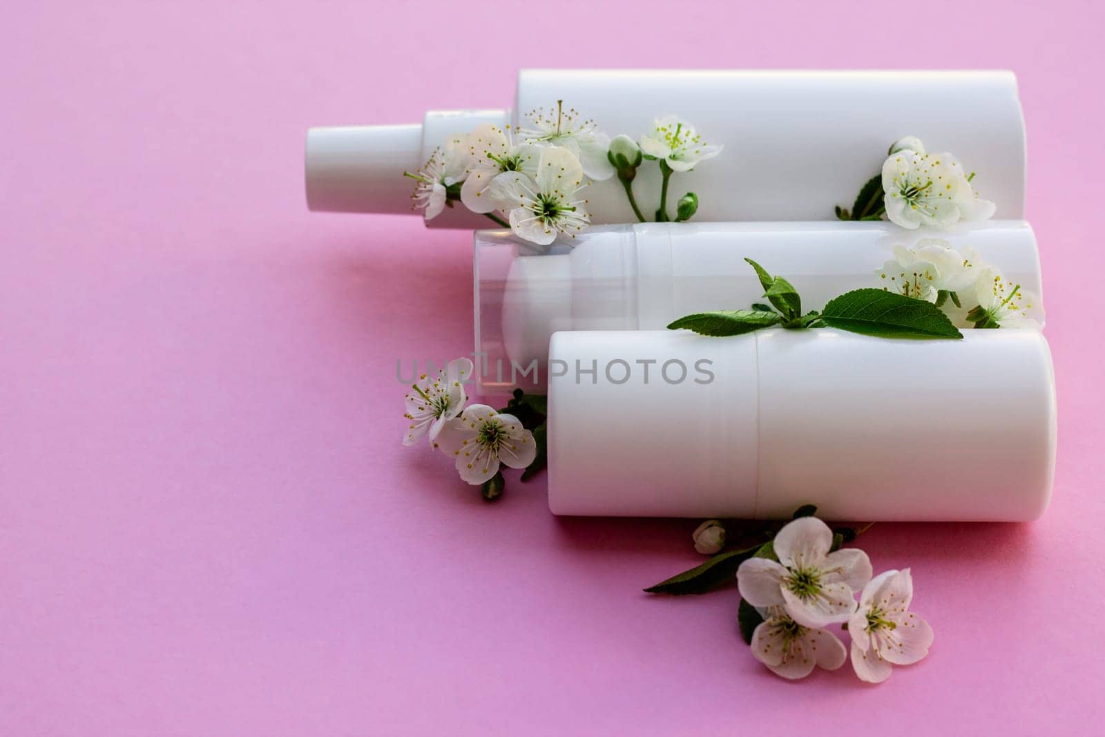 White cosmetic bottles, bath bomb, handmade soap, bath salt, massage brush, sponge, cotton buds with cherry flowers on a pink background. Natural organic cosmetics concept.