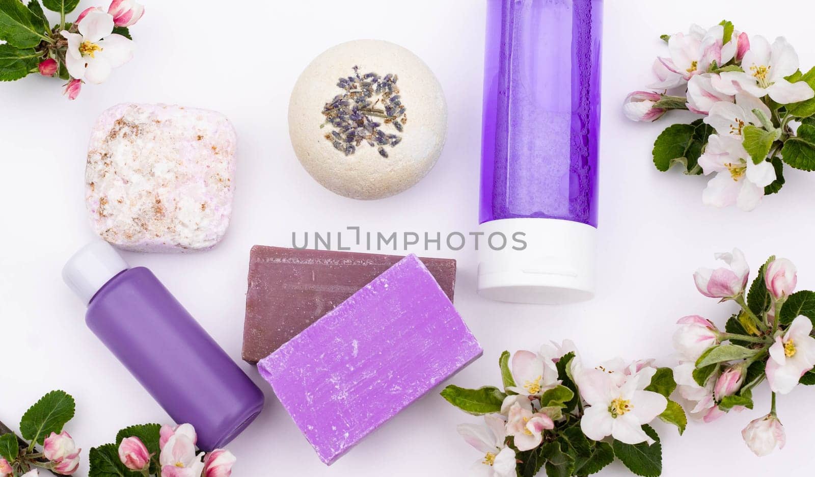 Top view. Lilac cosmetic bottles, bath bomb, handmade soap, bath salt with pear flowers on a white background. Natural organic cosmetics concept. Flat lay