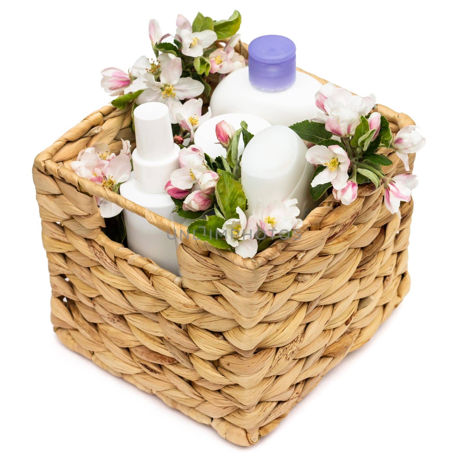 White cosmetic bottles in a wicker basket with pear flowers isolated on a white background. Natural organic cosmetics concept