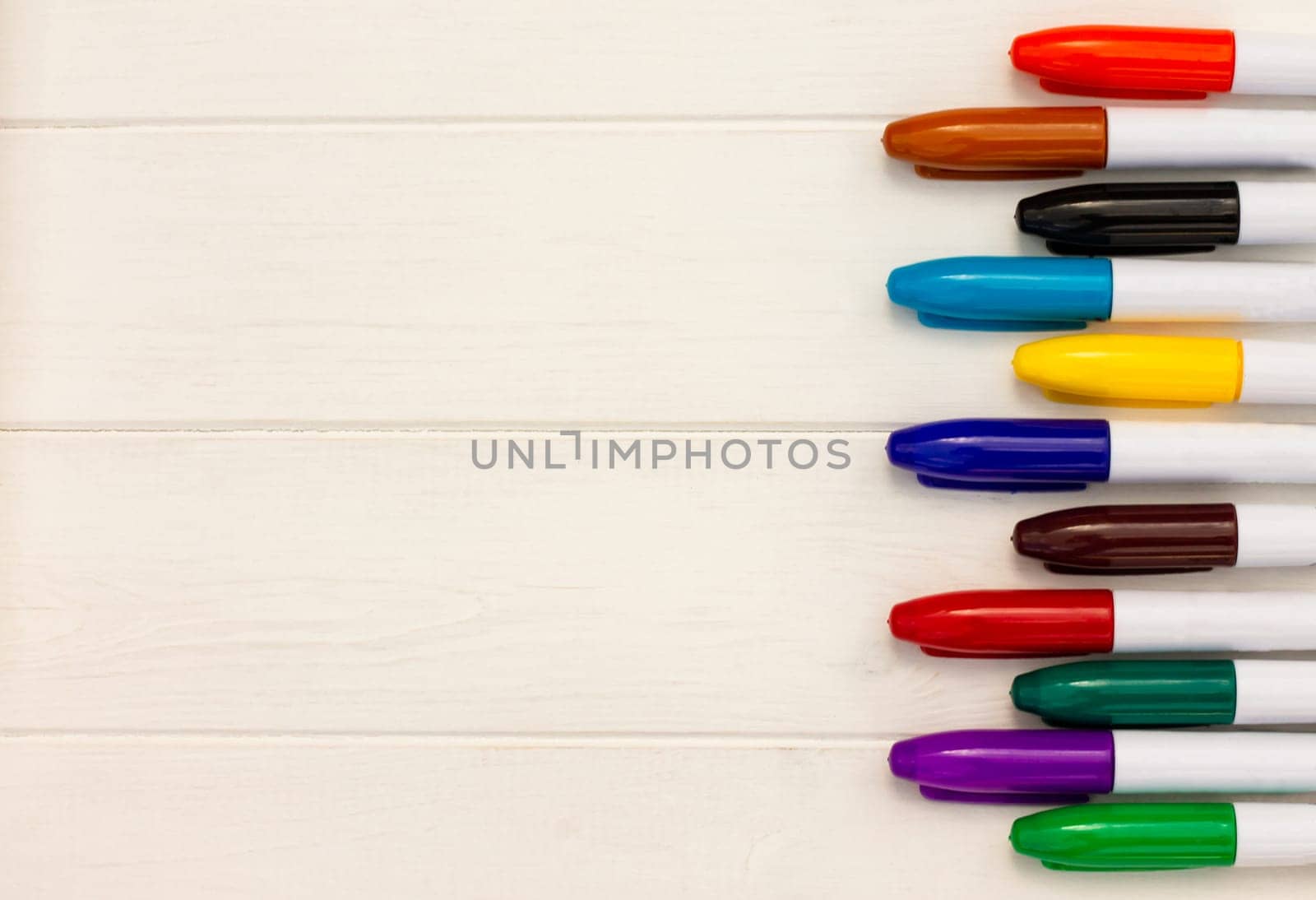 Multi-colored markers on a white wooden background. Top view. Copy space