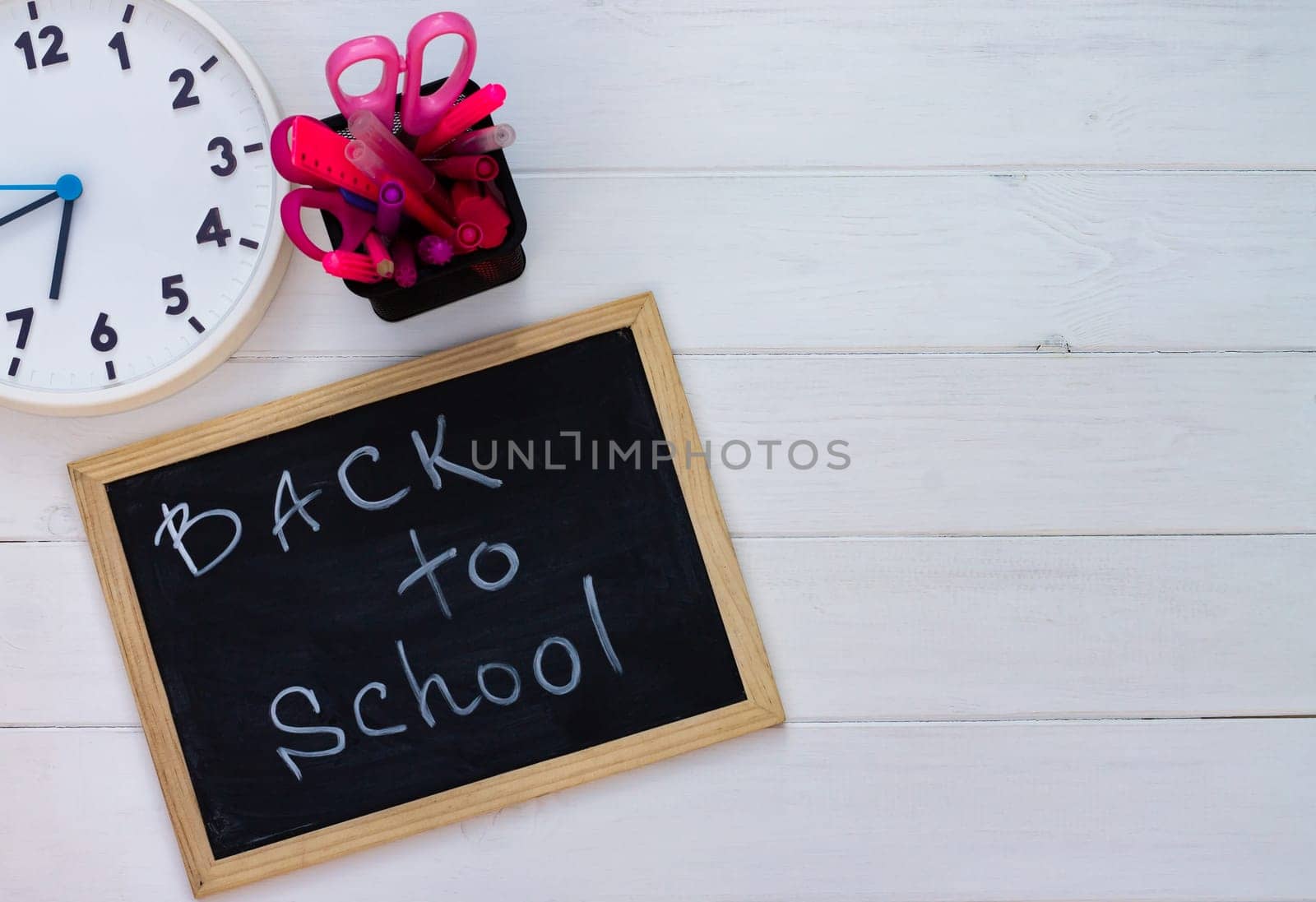 Back to school black chalk board on a white wooden background, pink supplies. Top view. Copy space. Education concept.