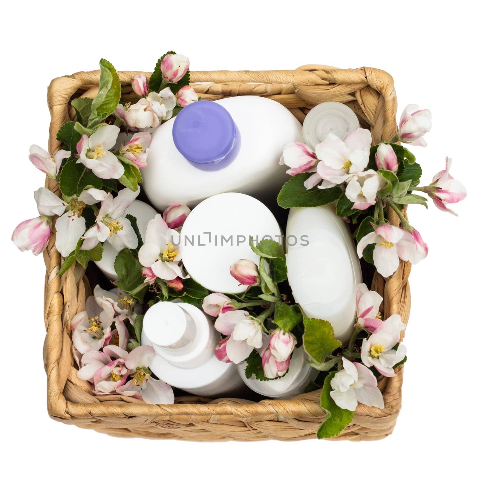 White cosmetic bottles in a wicker basket with pear flowers isolated on a white background. Natural organic cosmetics concept. Top view
