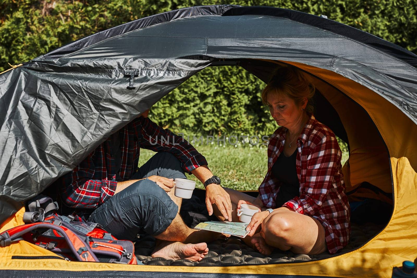 Couple planning next trip while sitting with map in tent. People relaxing in tent at camping during summer vacation. Actively spending vacations outdoors close to nature. Concept of camp life