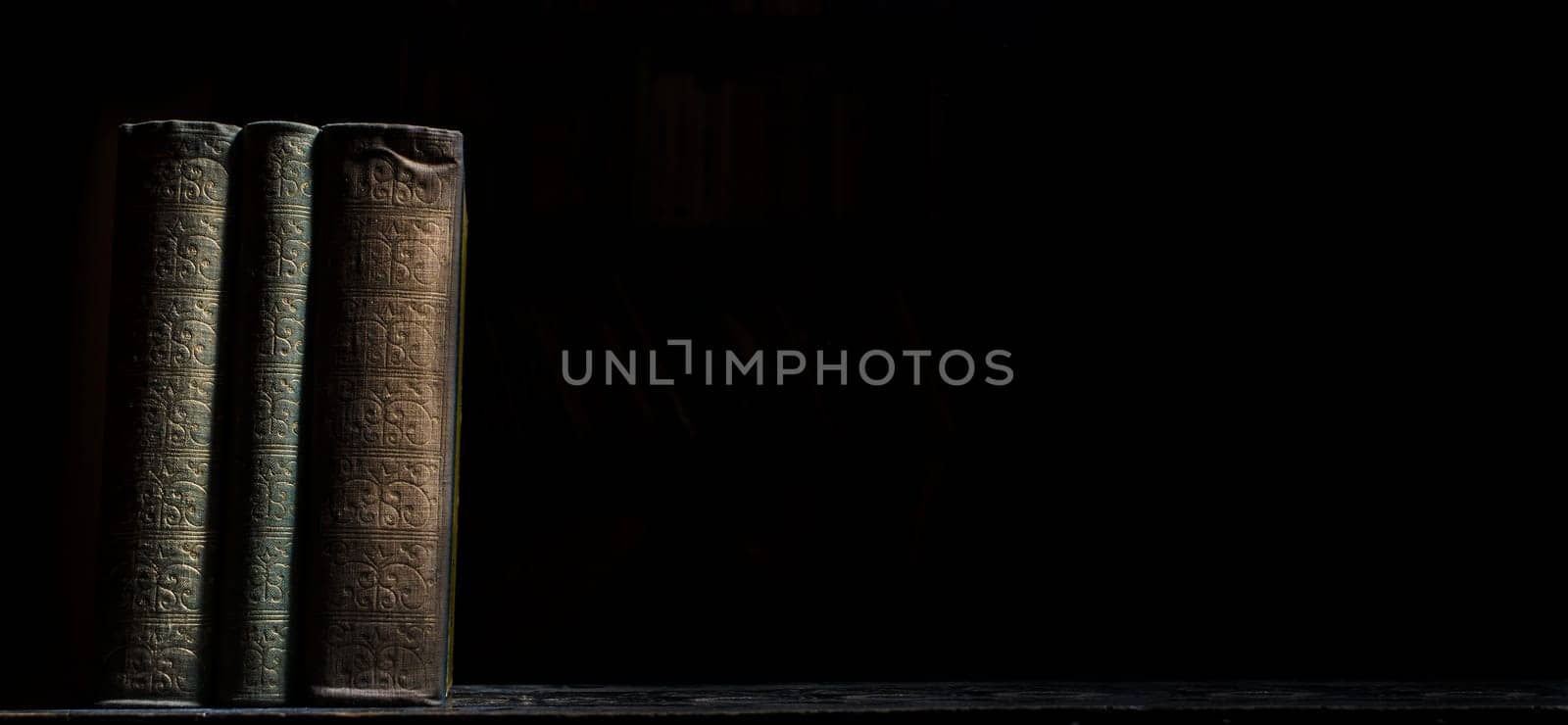 Old book on wooden bookshelf over black background. Vintage book covers still life on dark backdrop. University education study.