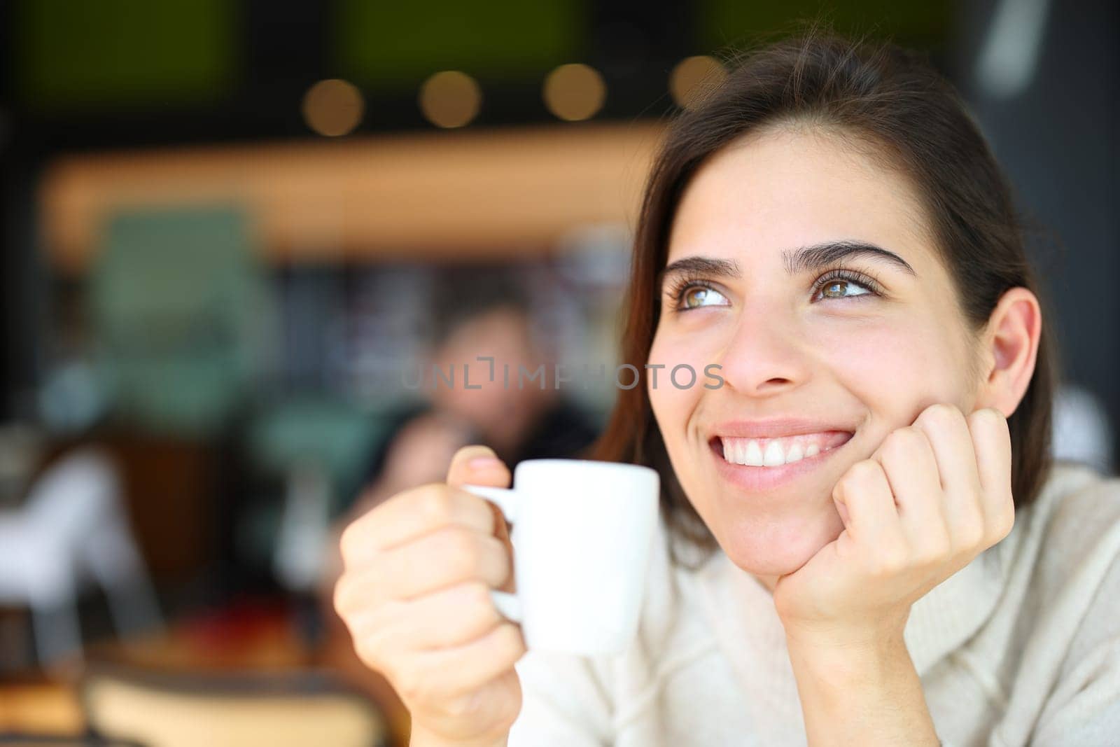 Happy woman dreaming drinking coffee in a restaurant
