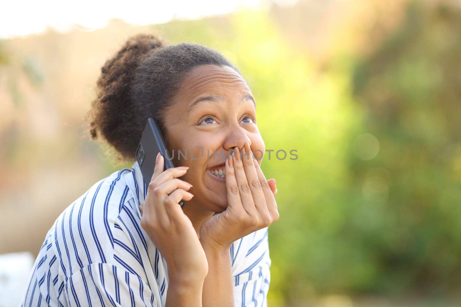 Funny black woman calling on phone in a park