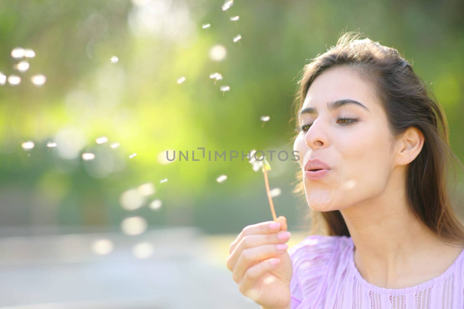 Happy woman blowing dandelion in spring in a park