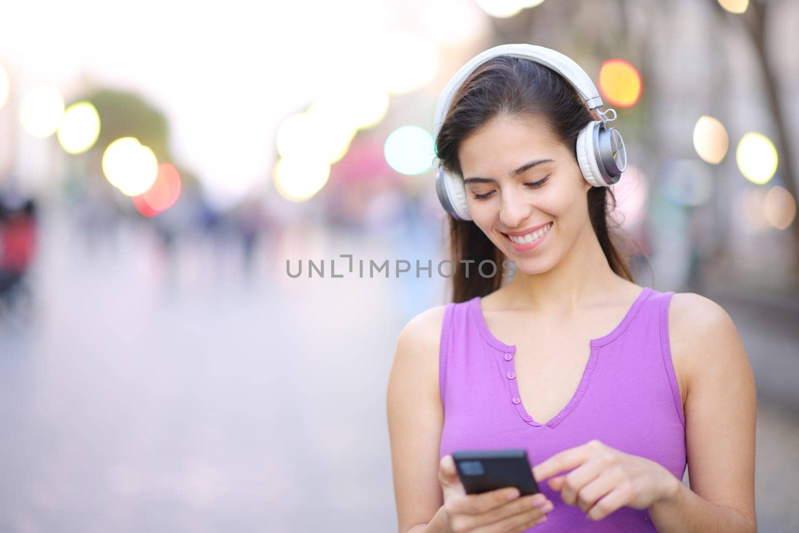 Happy woman wearing headphone in the street listening to music on phone