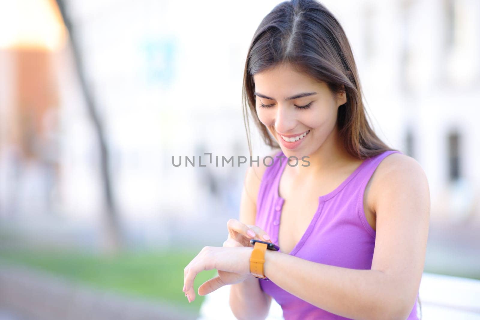 Happy woman using smartwatch sitting in the street