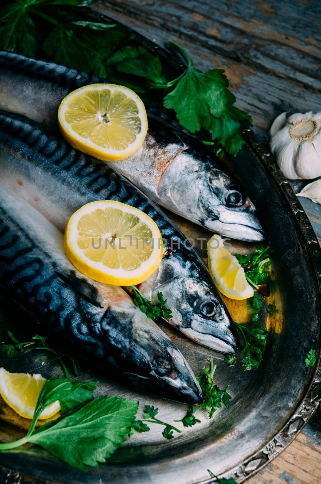 Fresh mackerel fish with lemon and spices served on silver plate from above. Homemade seafood dish recipe cooking. Healthy diet food prepared for dinner.