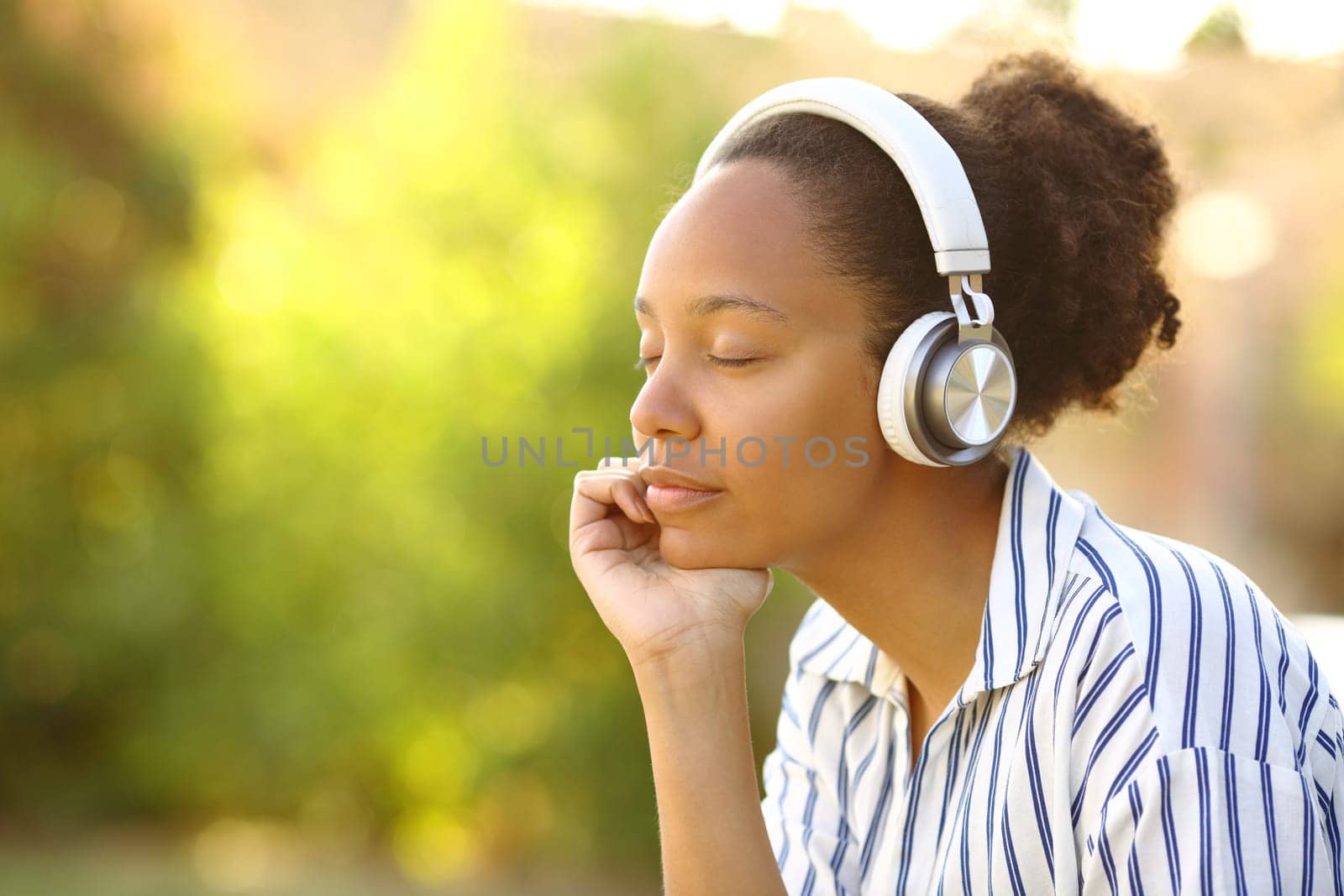 Relaxed black woman wearing headphone listening music resting in a park