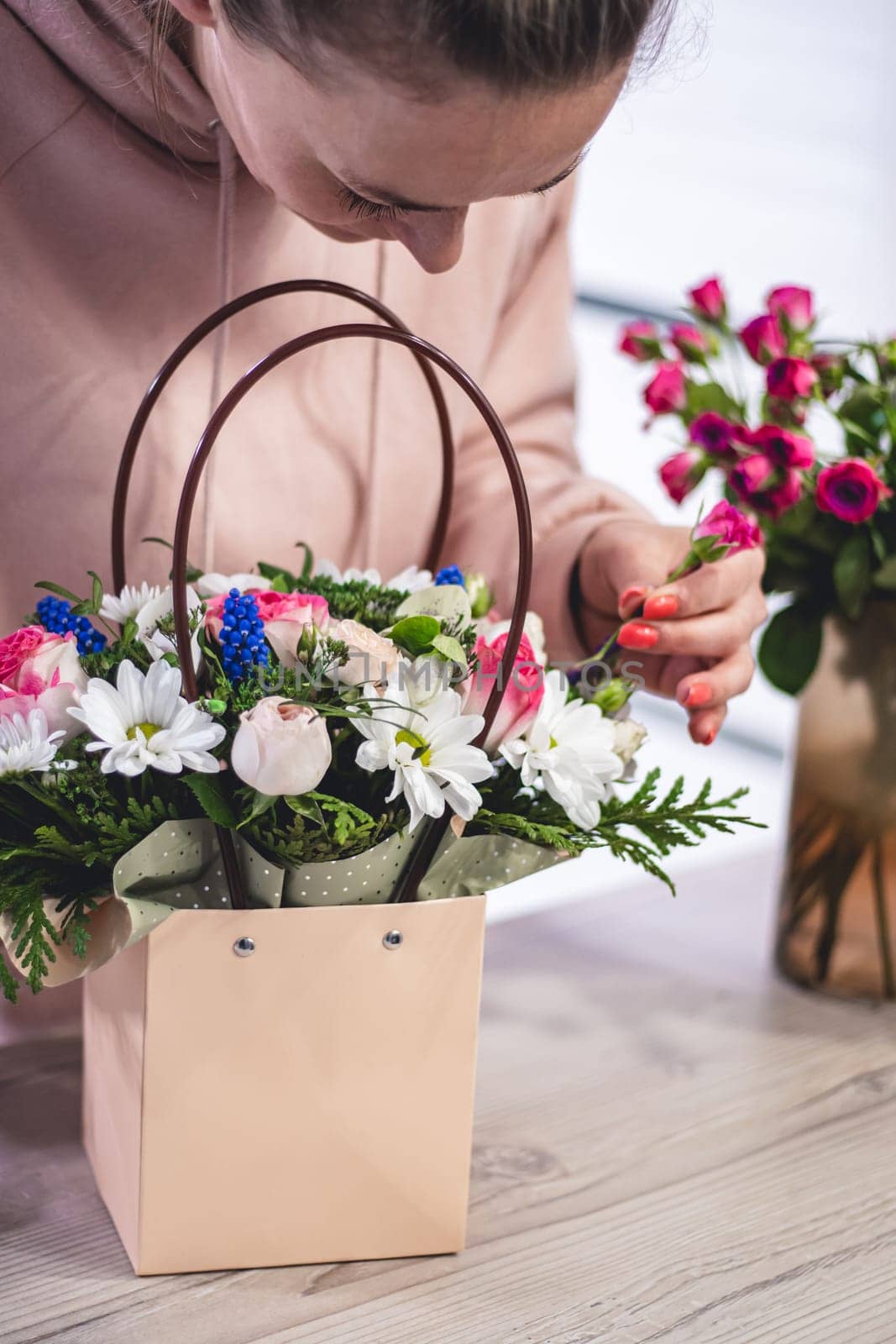 Female picking up bouquet of different flowers in paper gift bag with handles, vertical