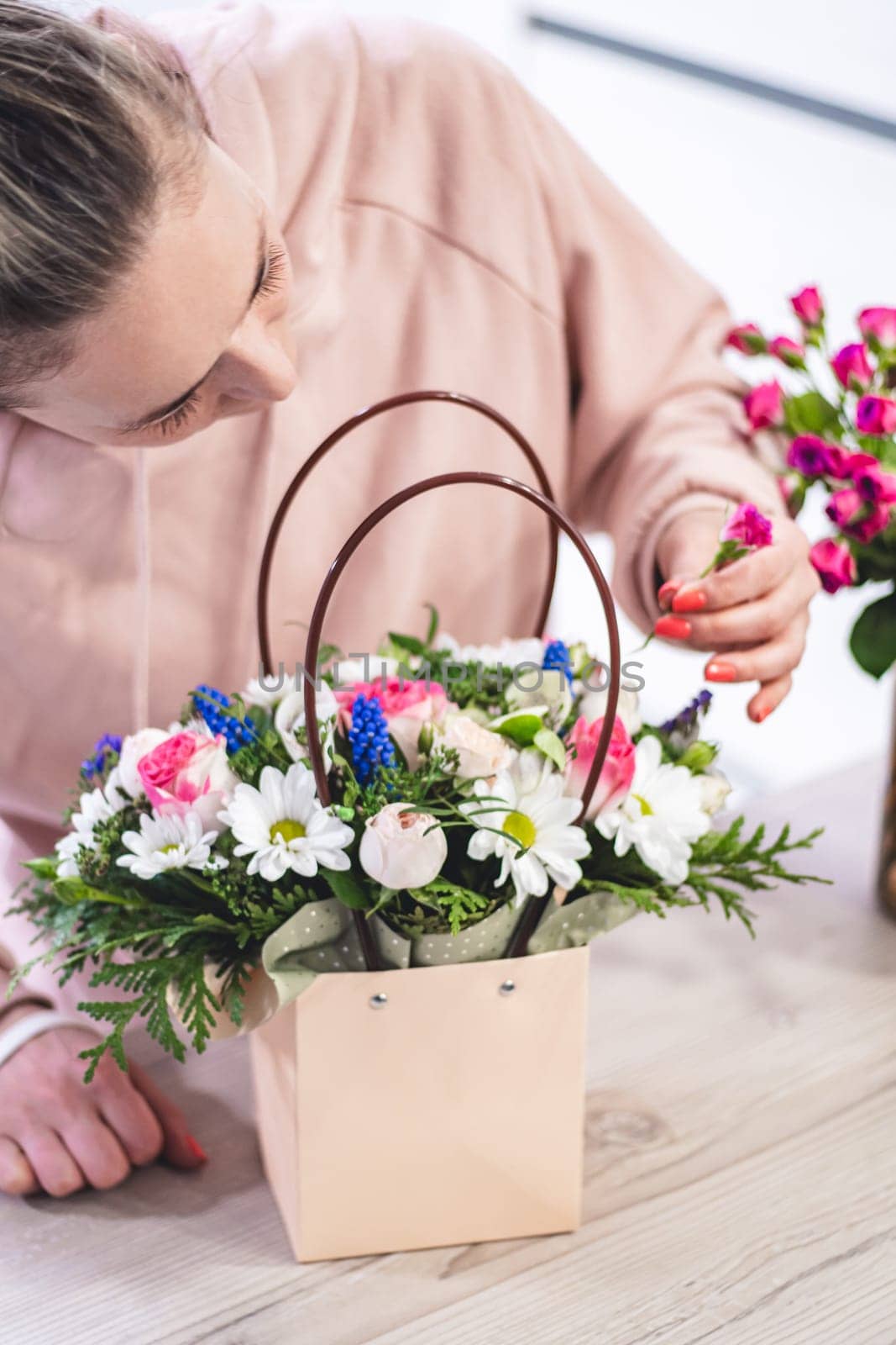 Female picking up bouquet of different flowers in paper gift bag with handles, vertical