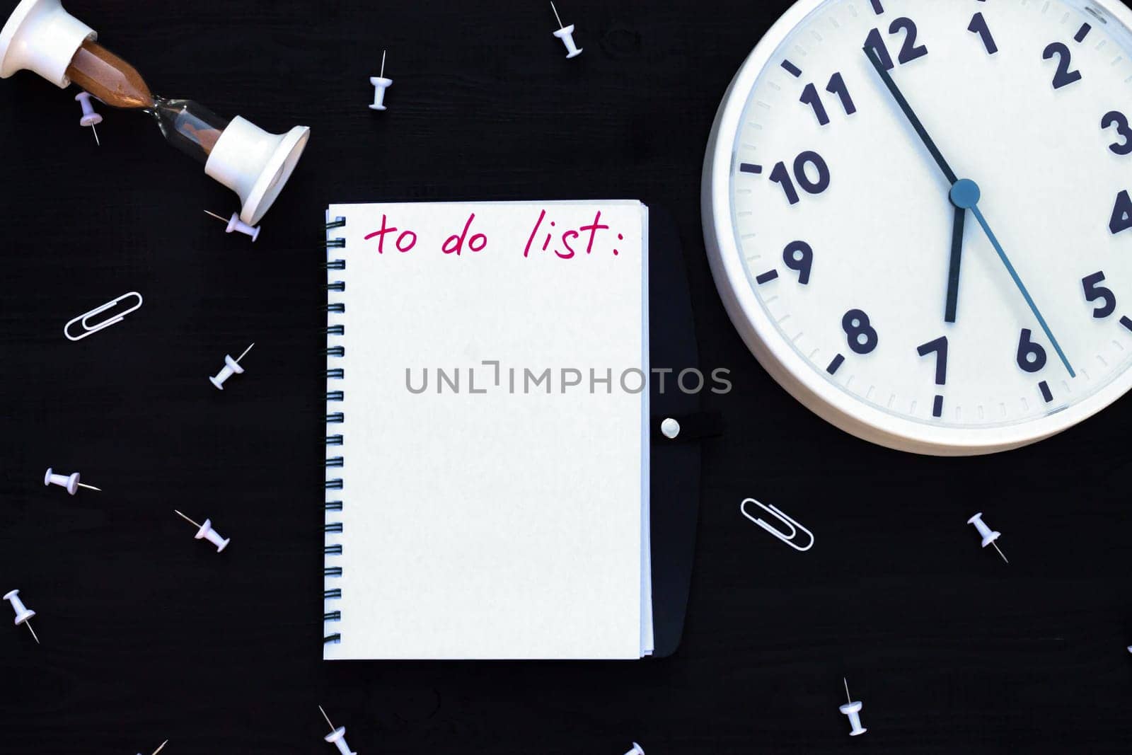 Notebook with To Do List on a black wooden background with clock and hourglass, paper clips. Top view. Copy space
