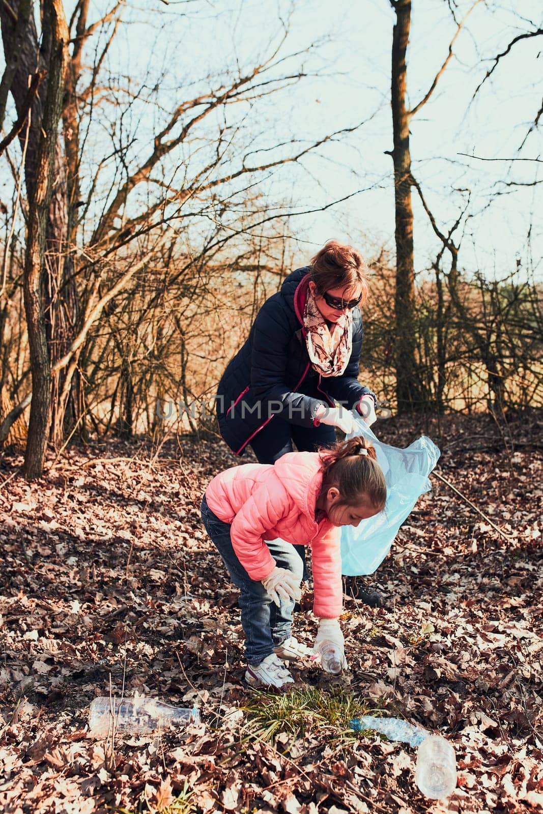 Family cleaning up a forest. Volunteers picking plastic waste to bags. Concept of plastic pollution and too many plastic waste. Environmental issue. Environmental damage. Responsibilitiy for environment. Real people, authentic situations