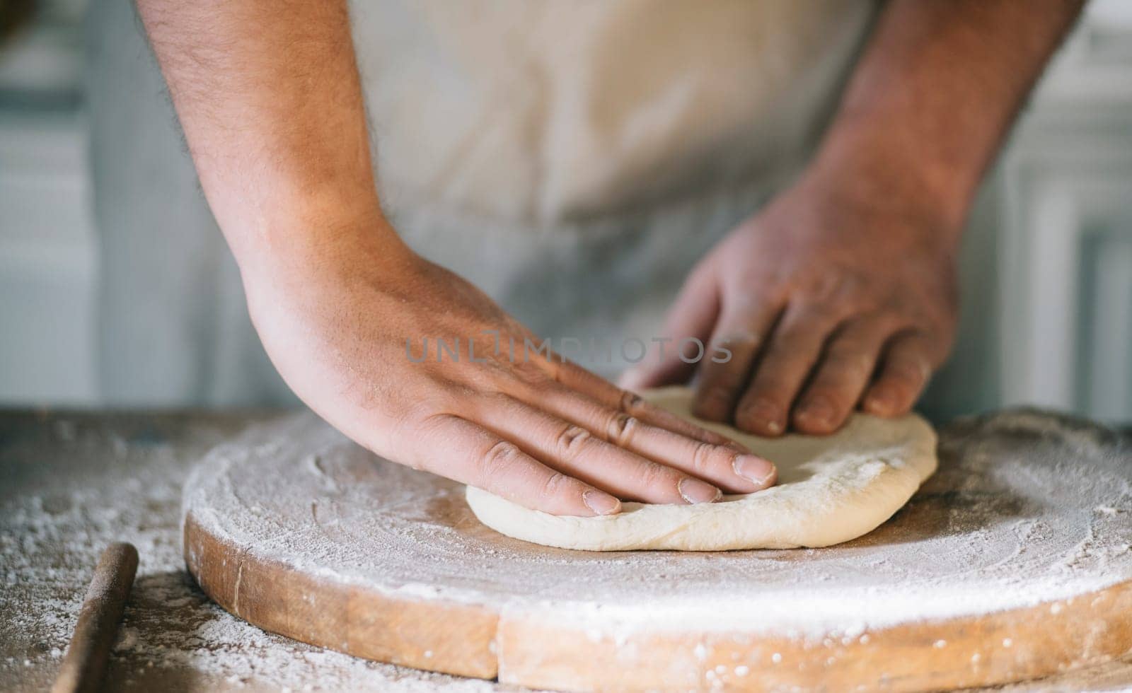 Man kneading and baking homemade pizza dough in the kitchen. Closeup on baker's hands preparing loaf of bread. Cooking and food preparation at home.