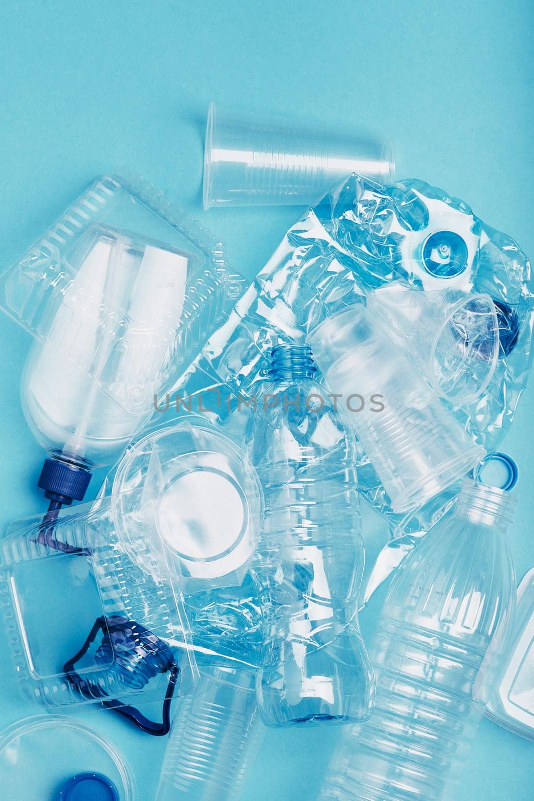 Squashed empty plastic bottles, cups, packagings, market bags  and caps over blue background. Collecting plastic waste to recycling. Concept of plastic pollution and too many plastic waste. Copy space at the top