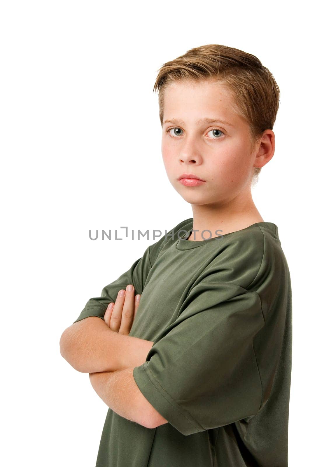 Side torso portrait of a young male teenager in a t-shirt and arms crossed against a white background looking seriously at the camera.