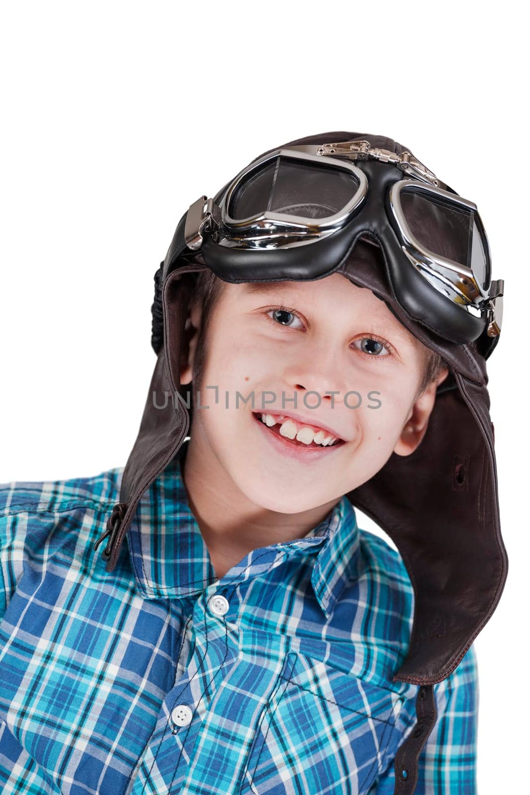 Frontal head and shoulders view of a Caucasian 10 year old boy wearing an attached leather cap and traditional motorcycle goggles against a white background looking happily at the camera.