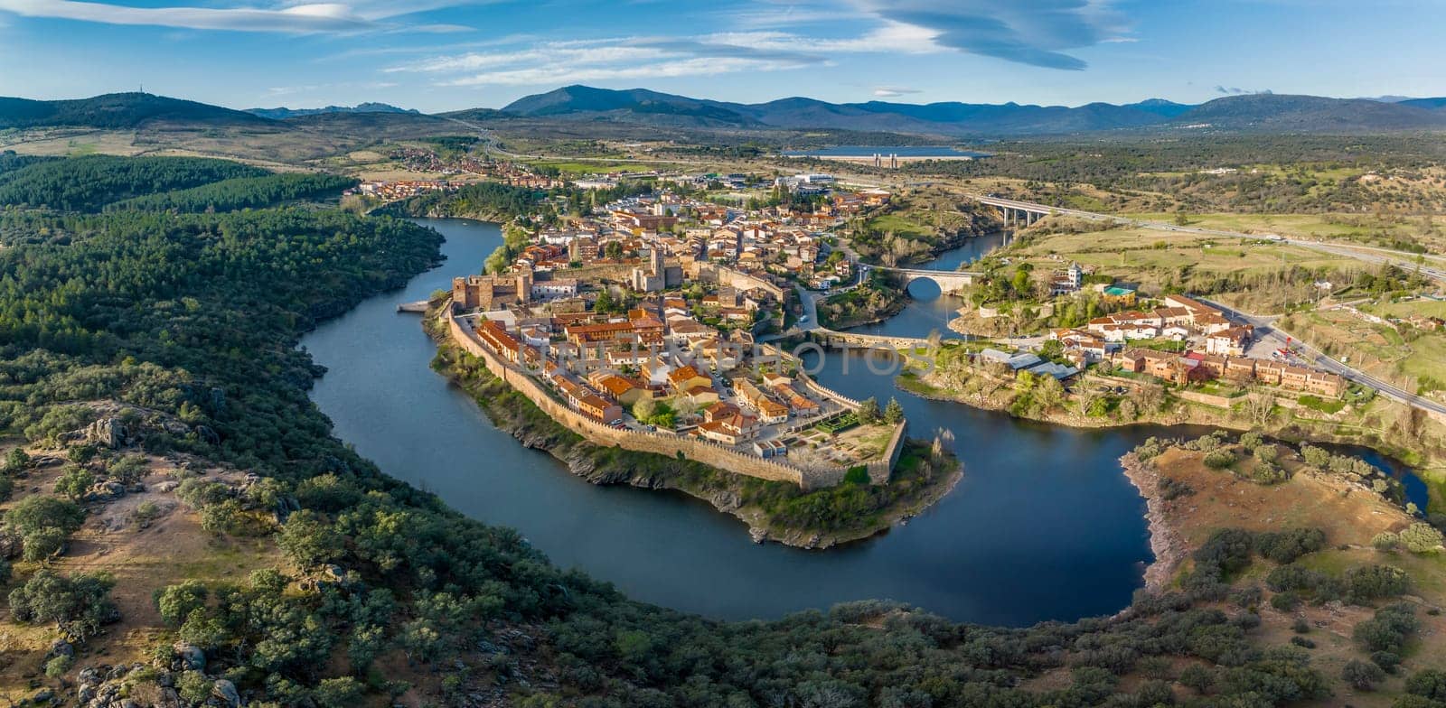 Aerial view of Buitrago del Lozoya, a well preserved historic village near Madrid, surrounded by the Lozoya river, with the Guadarrama mountain chain and reservoir in the background.