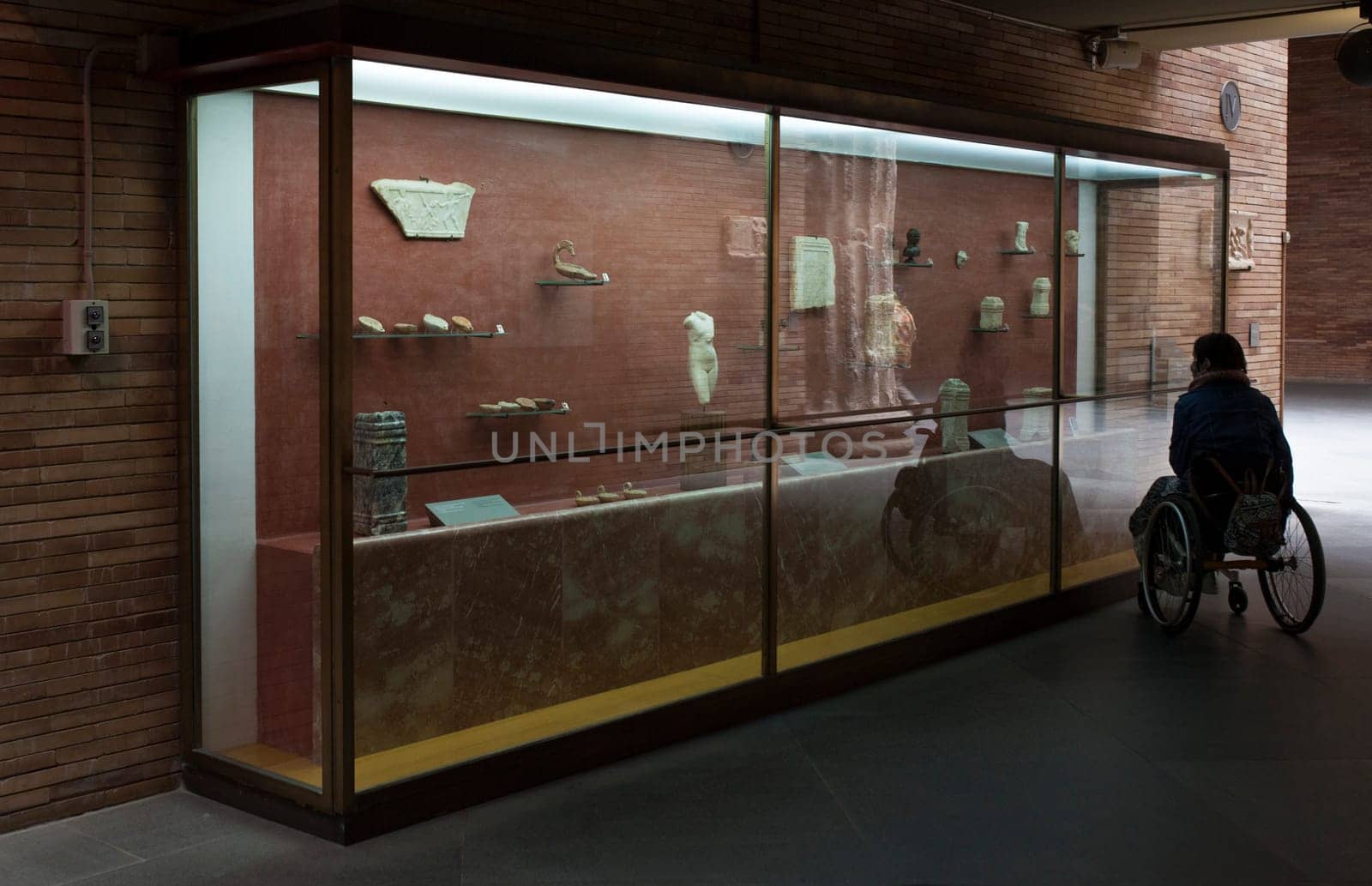Merida, Spain - May 23th, 2021: Woman in a wheelchair iobserves glass cabinet at National Museum of Roman Art in Merida, Spain