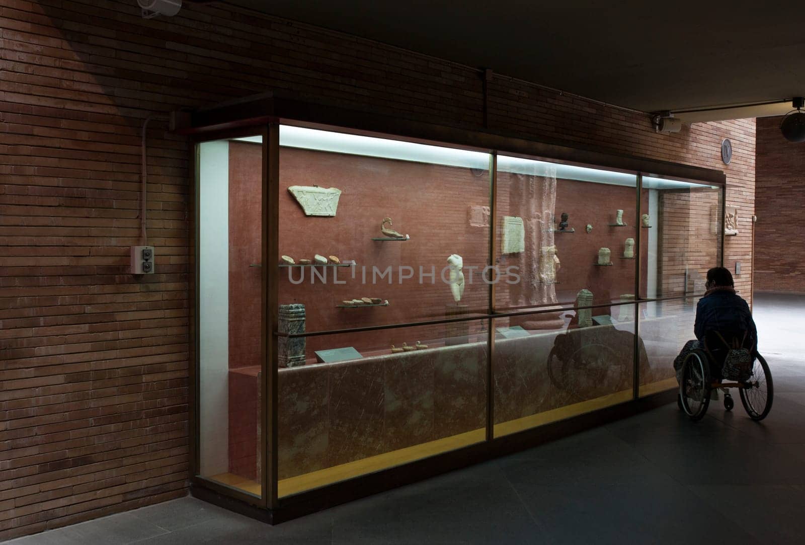 Merida, Spain - May 23th, 2021: Woman in a wheelchair iobserves glass cabinet at National Museum of Roman Art in Merida, Spain