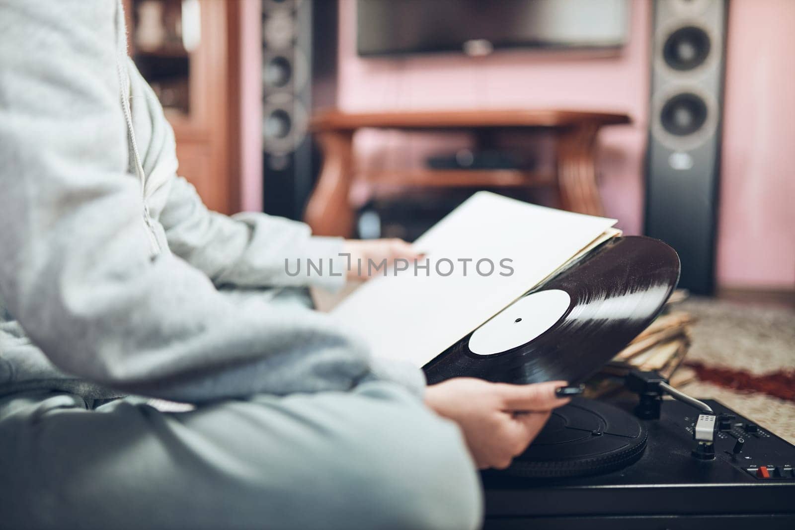 Young woman listening to music from vinyl record player. Retro and vintage music style. Girl holding analog record album sitting in room at home. Female enjoying music from old record collection