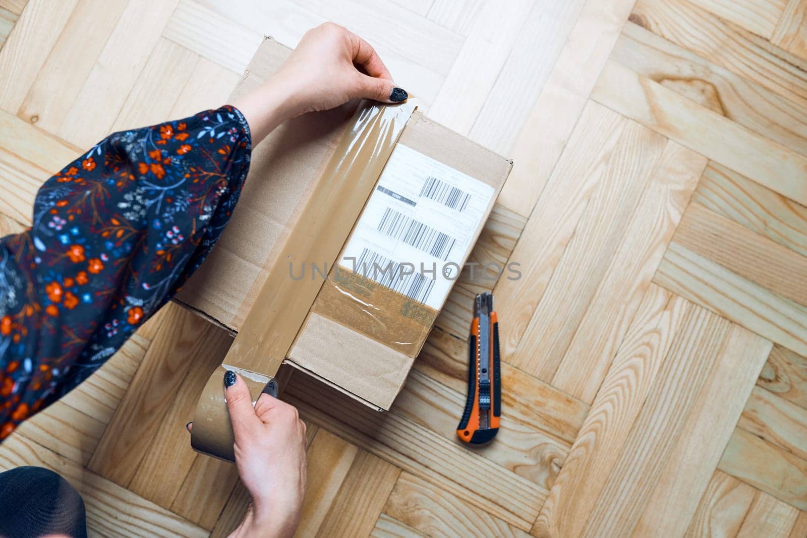 Woman preparing online order. Packing parcel to send using cardbox, tape and knife