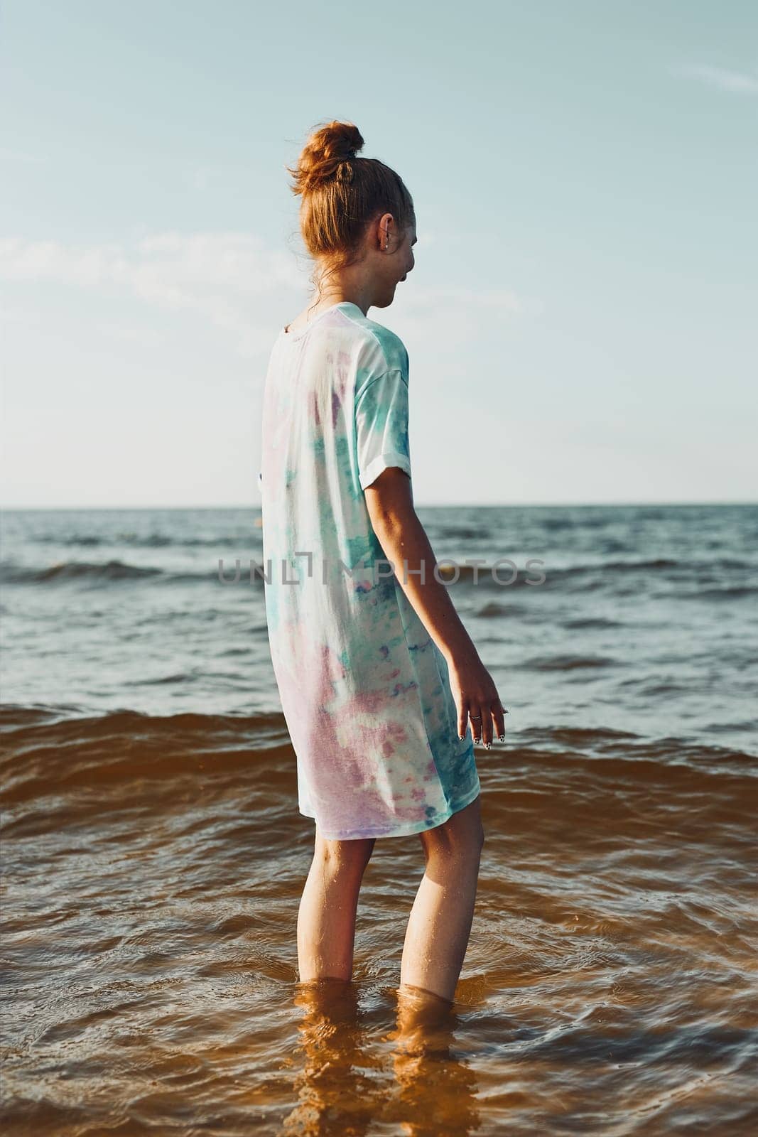 Girl standing in a water spending a free time on a beach over a sea at sunset during summer vacation