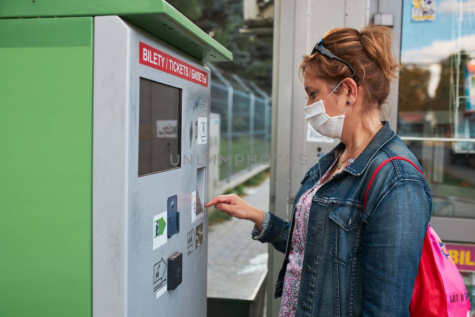 Woman buying bus ticket in ticket machine wearing face mask to cover mouth and nose traveling during pandemic coronavirus outbreak