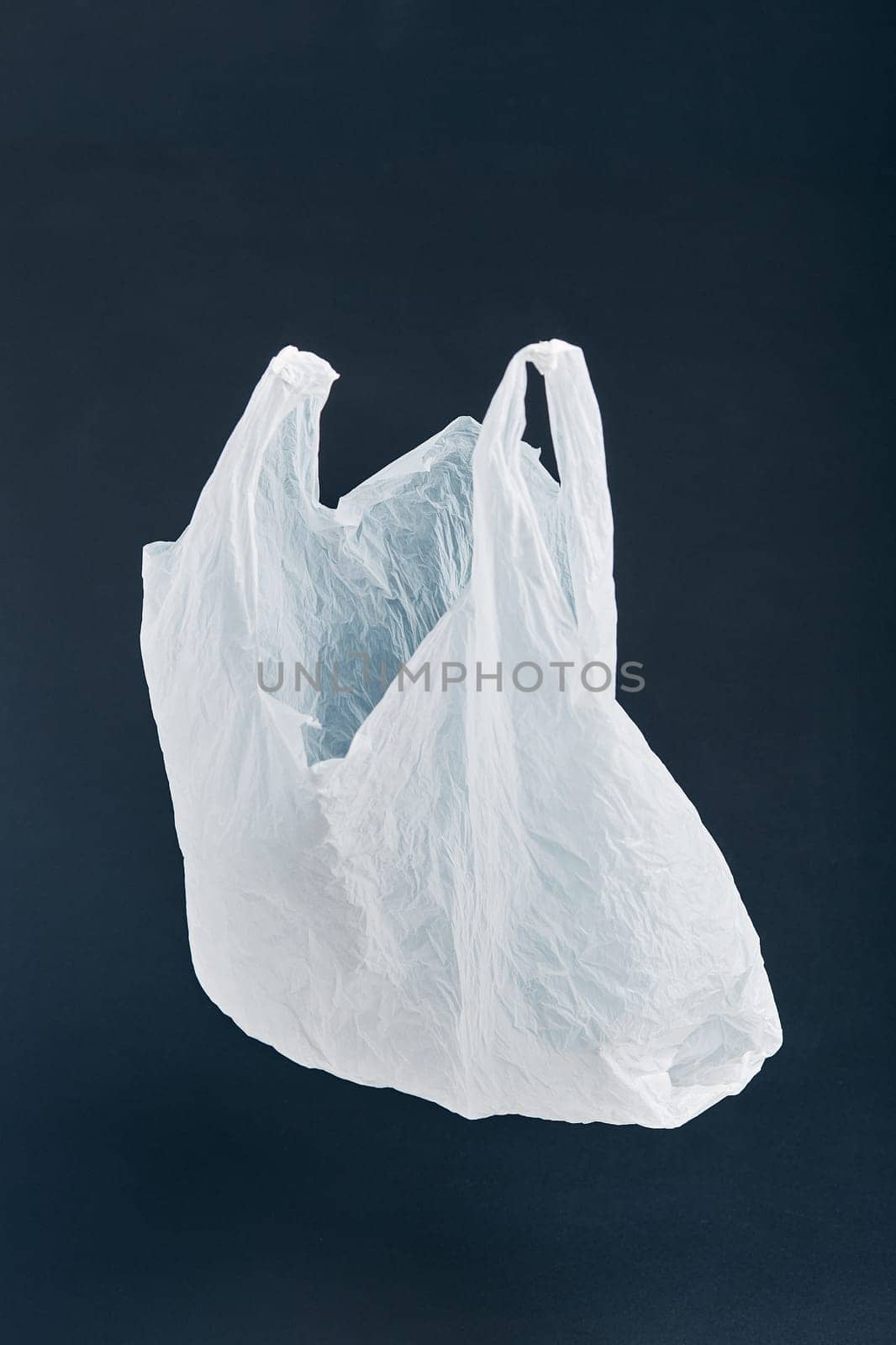 White empty plastic bag floating over black background. Collecting plastic waste to recycling. Concept of plastic pollution and too many plastic waste. Copy space at the top