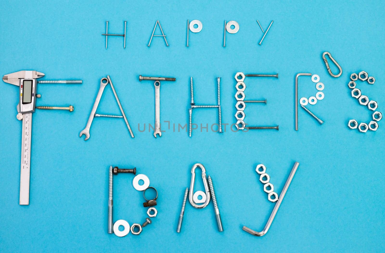 Text Happy Father's Day lined with bolts, nuts, wrenches and other construction tools on a blue background. Flat lay. Top view