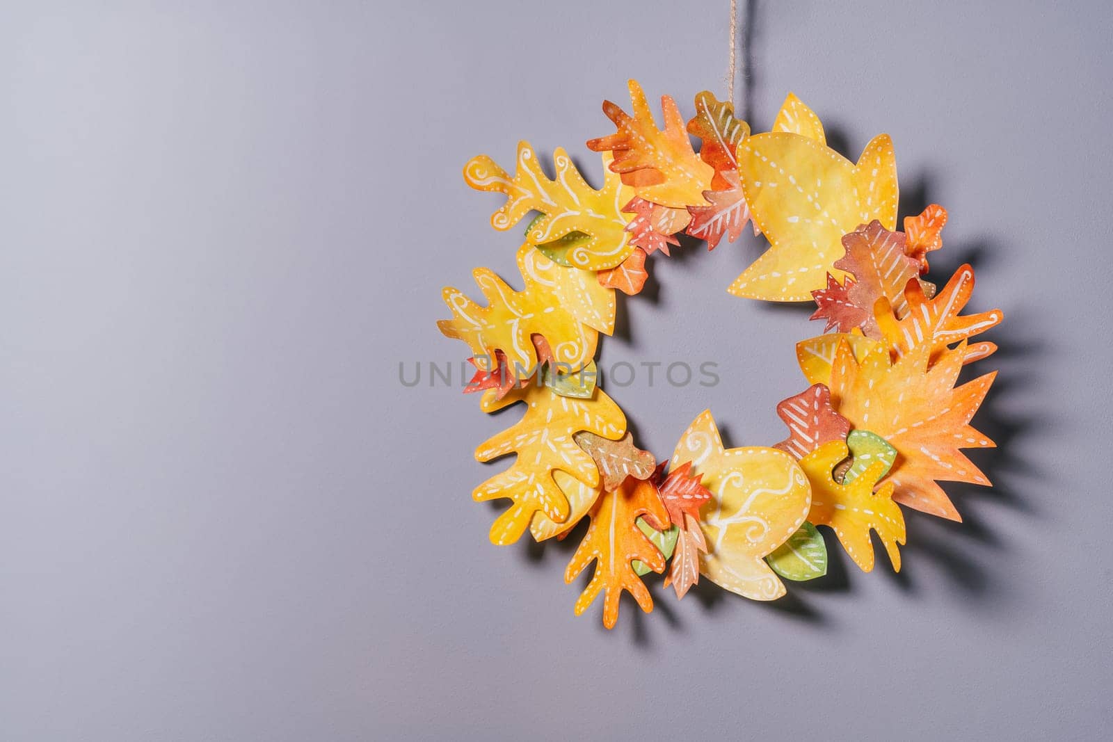 Homemade autumn yellow-red paper wreath on a gray wall background. Seasonal DIY