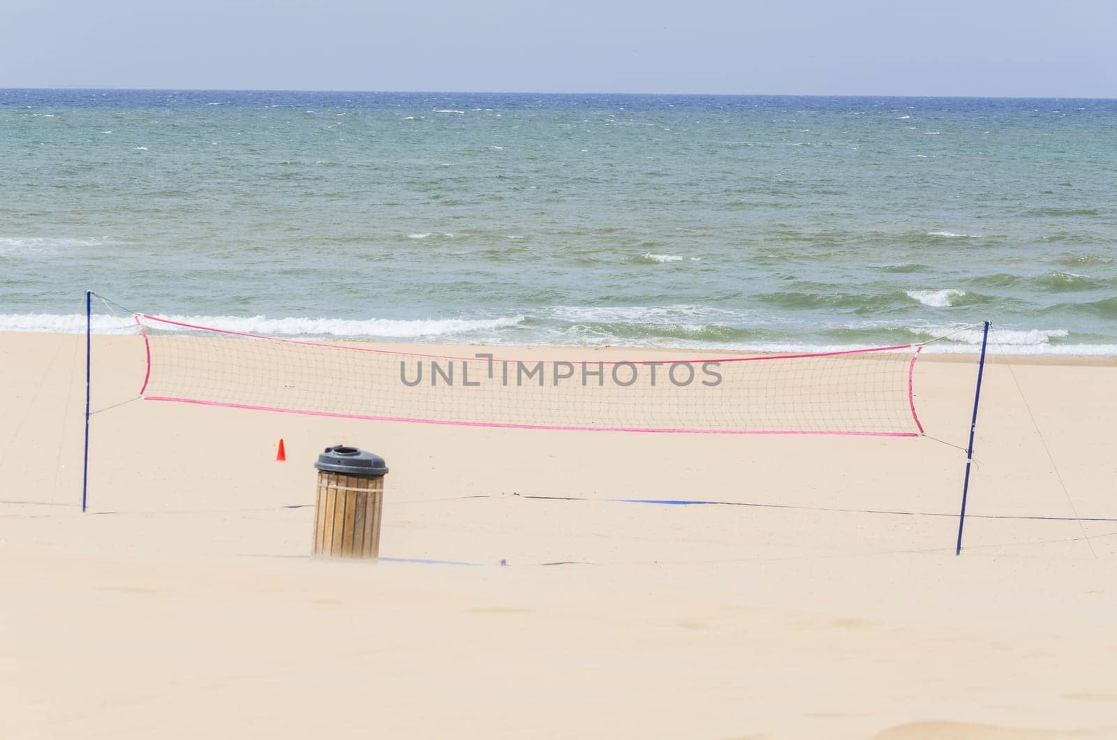 Beach a volleyball net in the background the blue sea and a cloudless sky..
