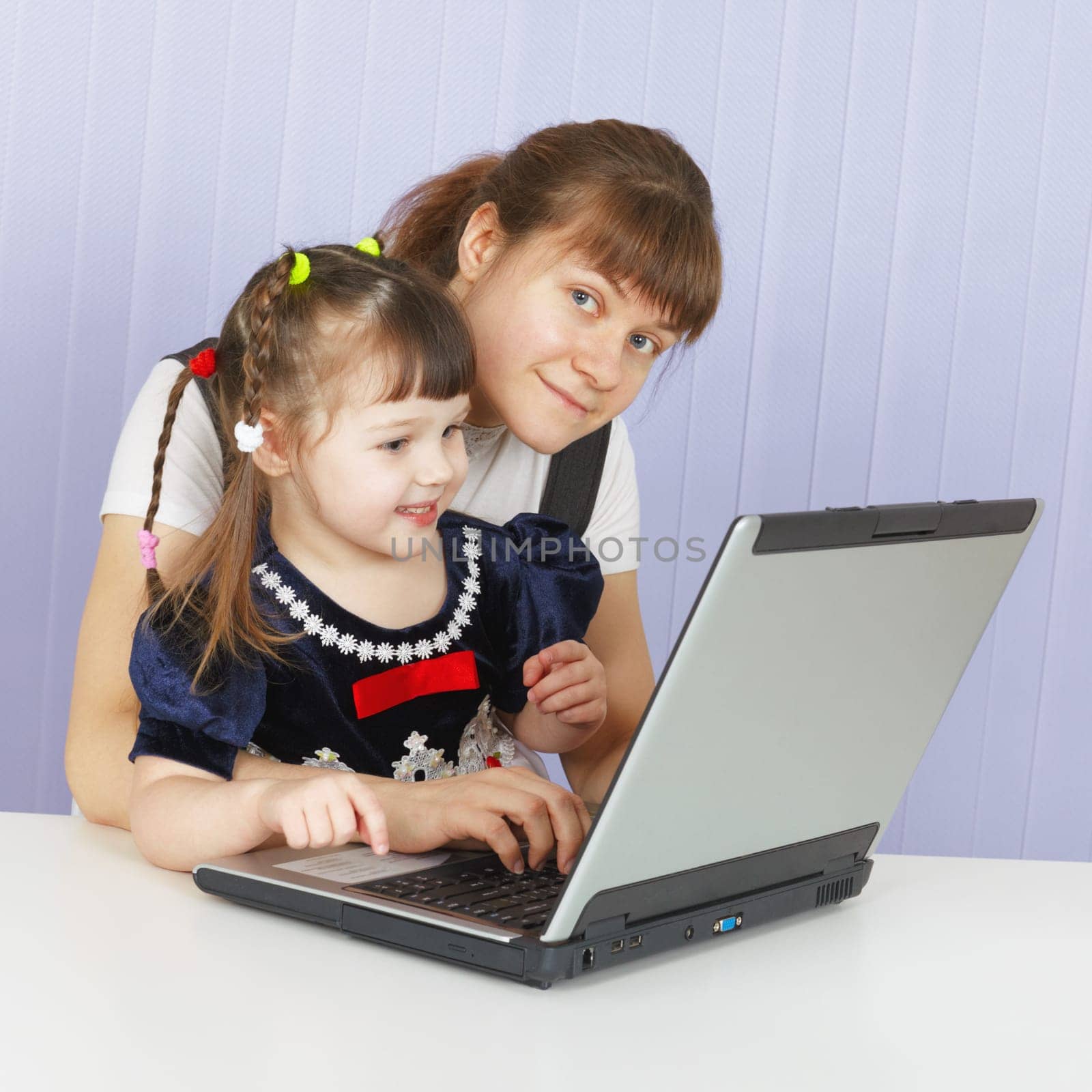 Mother and daughter playing with a computer at home sitting at the table