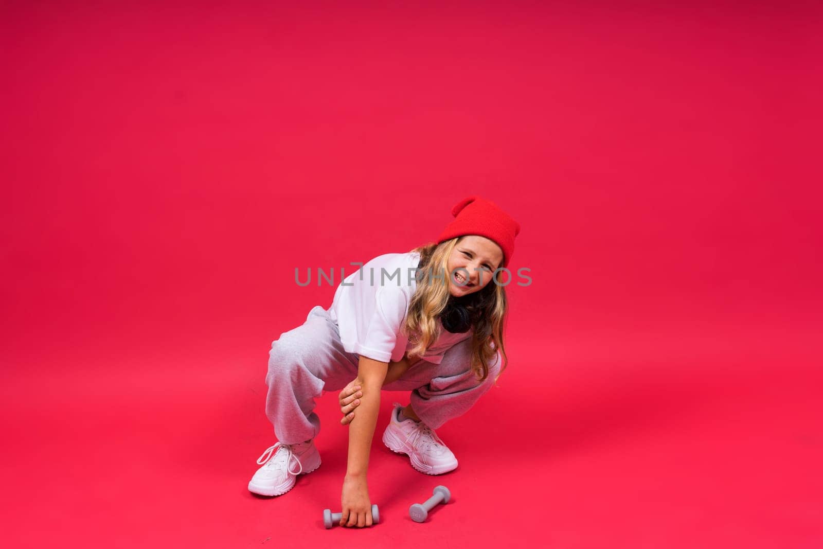 Kid girl doing fitness exercises with dumbbells on a red background